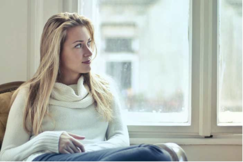 blonde woman in white sweater looking out a window