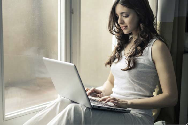 Dark-haired+woman+wearing+white+clothes+using+a+laptop+while+sitting+in+a+window