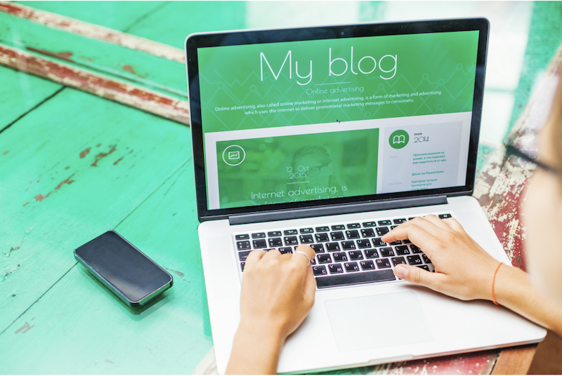 closeup of person typing on a laptop with a phone next to them on a green table
