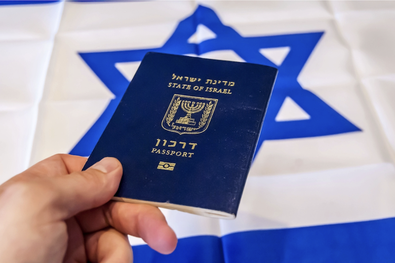 hand holding Israeli passport in front of national flag of Israel