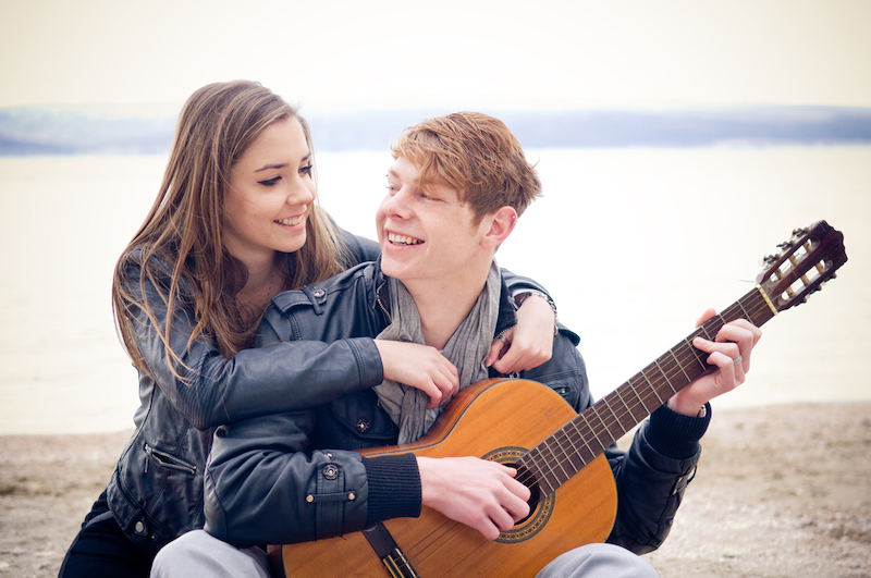 Young woman with her arms around young man with acoustic guitar on the beach