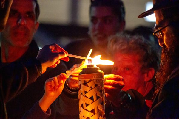 Rabbi Chaim Brook (R) and other members from the local Jewish community gather around a torch to light their candles for Chabad at CSUNs annual menorah lighting in front of the University Library in Northridge, Calf., on Dec. 7, 2023.