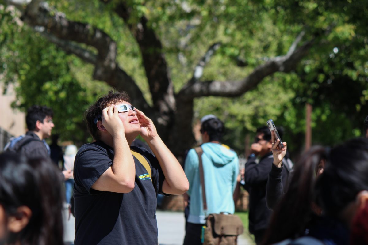Film major Christopher Hernandez holds up viewing glasses and looks up at the partial solar eclipse on the lawn in front of the Donald E. Bianchi Planetarium at California State University, Northridge in Northridge, Calif., on April 8, 2024.