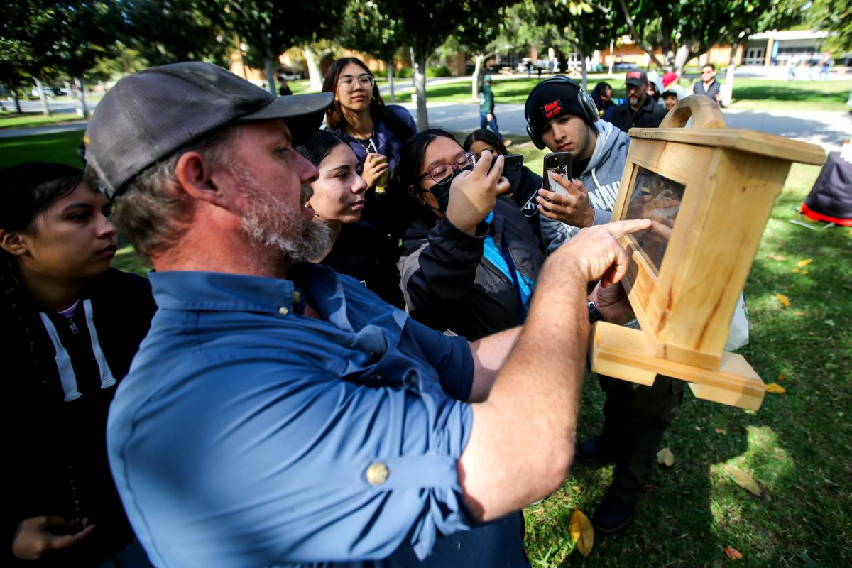 Beekeeper Keith Roberts shows off bees in their hive to students waiting in line for honey tasting.