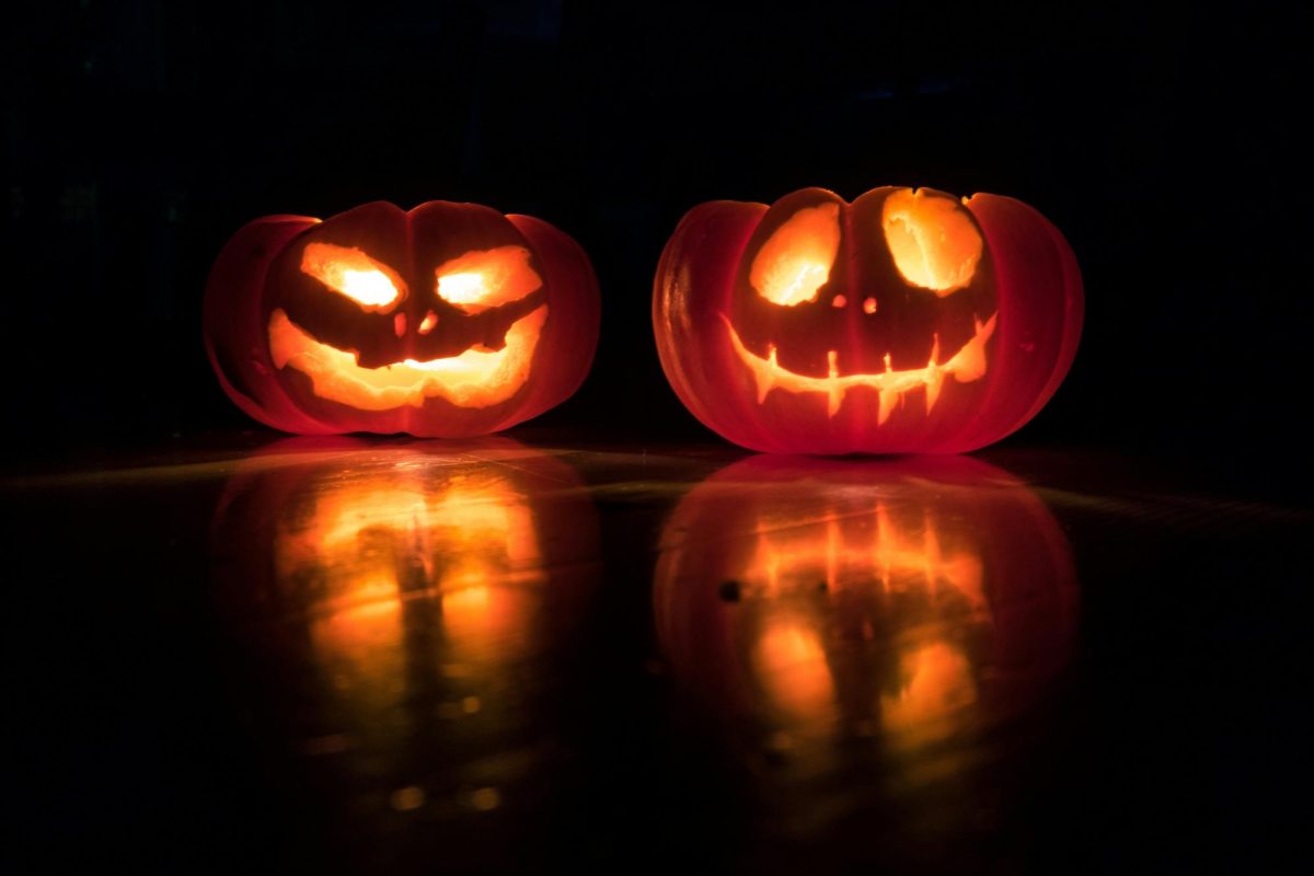 Two jack o' lanterns lit in the dark. Photo by David Menidry via Unsplash.