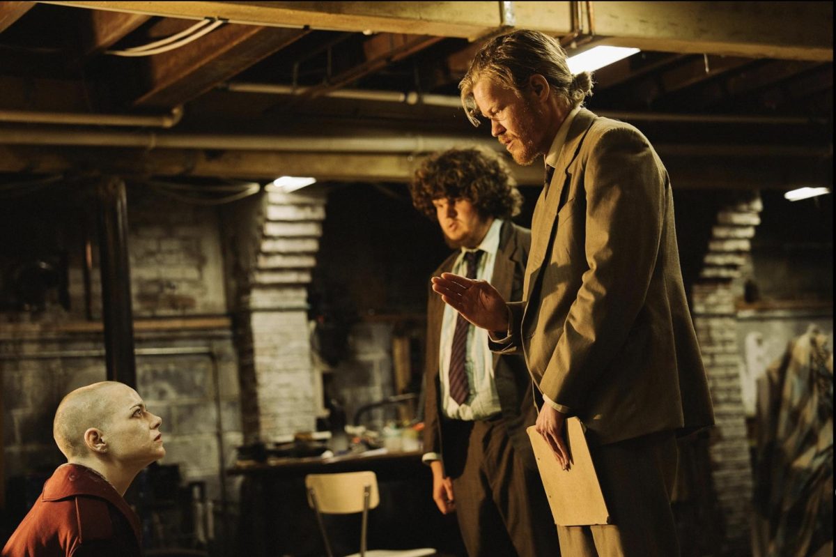 On the left, Emma Stone, looking up at Jesse Plemons and Aiden Delbis in "Bugonia" 2025.