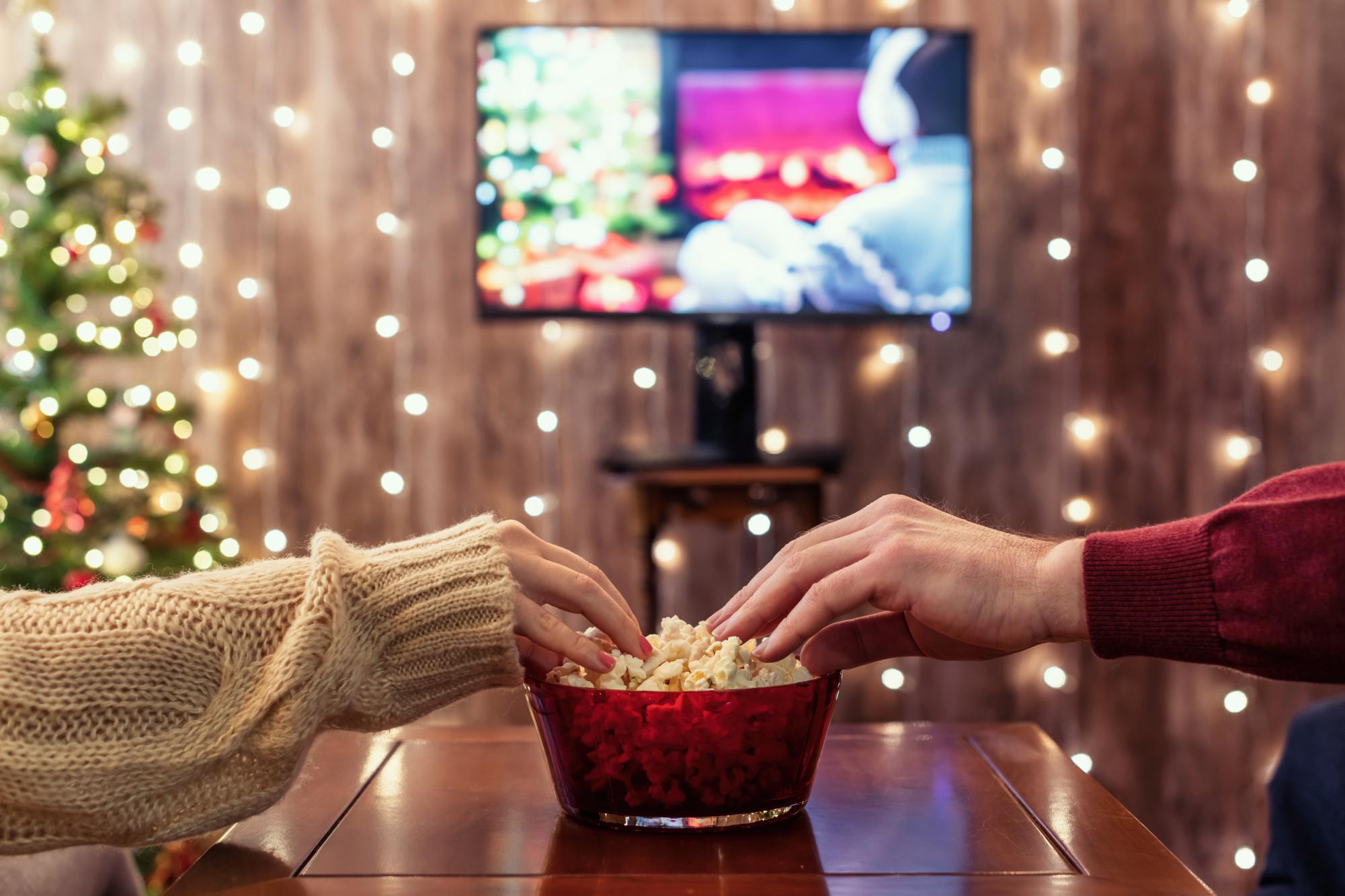 Couple watching tv and eating popcorn at their home cinema on Christmas Eve.
